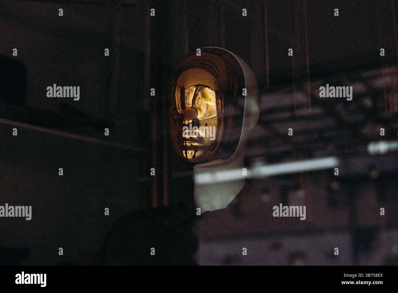 Una maschera dorata è collocata su uno sfondo scuro, riflettendo la luce e creando un'accattivante esposizione artistica. Il design elegante aggiunge un tocco di eleganza. Foto Stock