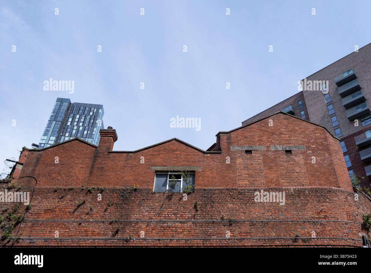 Guardando verso l'alto il vecchio edificio in mattoni rossi con nuovi edifici, appartamenti e hotel alle spalle. Manchester, Inghilterra, Regno Unito - 2025. Foto Stock