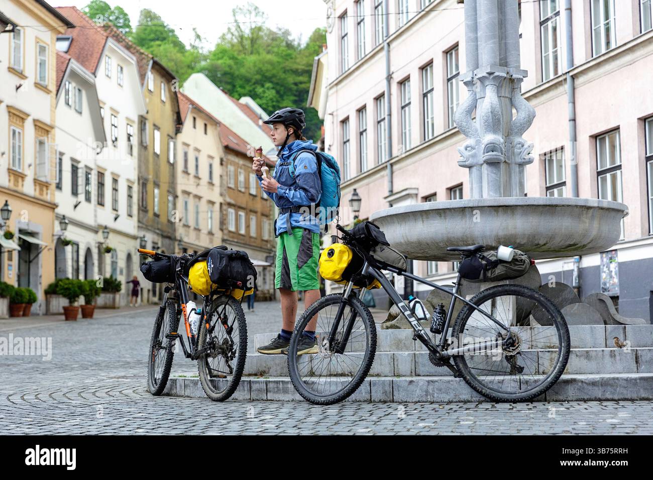 Adolescente in un viaggio in bicicletta in Slovenia, ciclista che si gusta un gelato presso una fontana di Ercole nella parte storica vecchia di Lubiana, Sloven Foto Stock