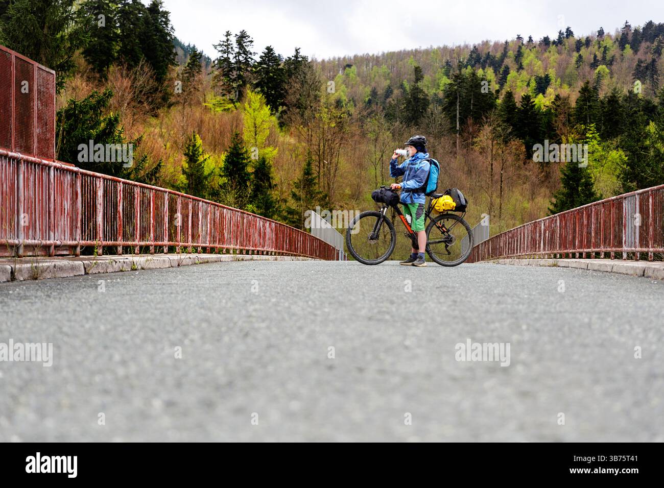Turista in un viaggio in bicicletta e bikepacking da Lubiana a Pirano in Slovenia, sorseggiando un drink su un ponte sull'autostrada nella regione di notranjska Foto Stock
