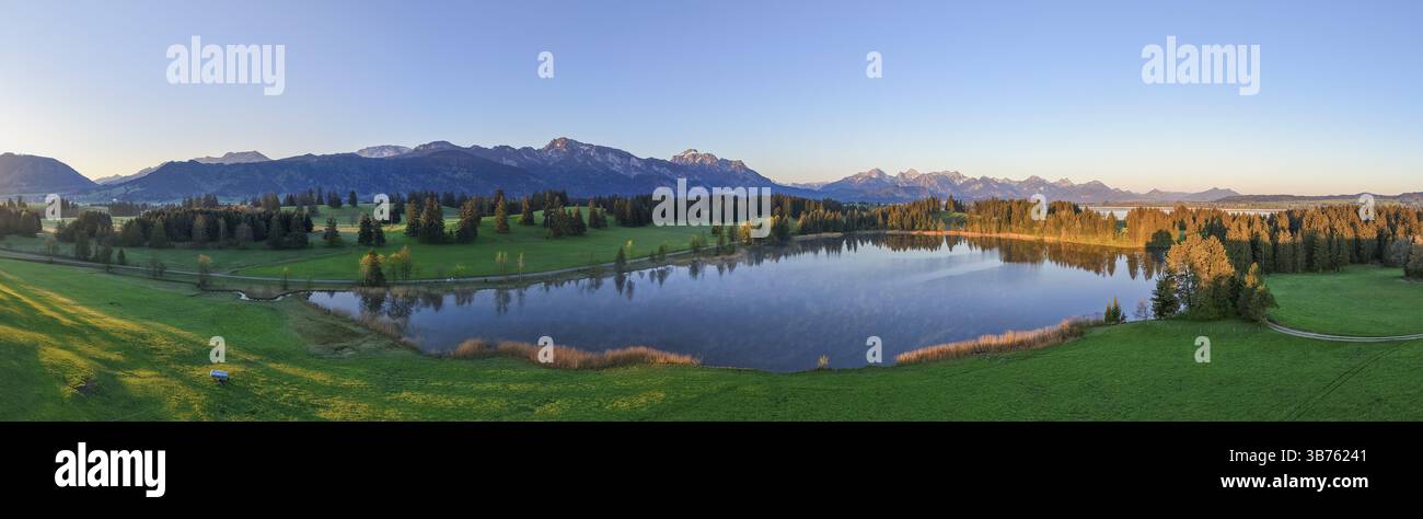 Vista panoramica di un lago circondato da foreste e montagne al tramonto, Hergratsrieder SEE, Alpi, vicino a Fuessen, Ostallgaeu, Allgaeu, Baviera, Germania Foto Stock