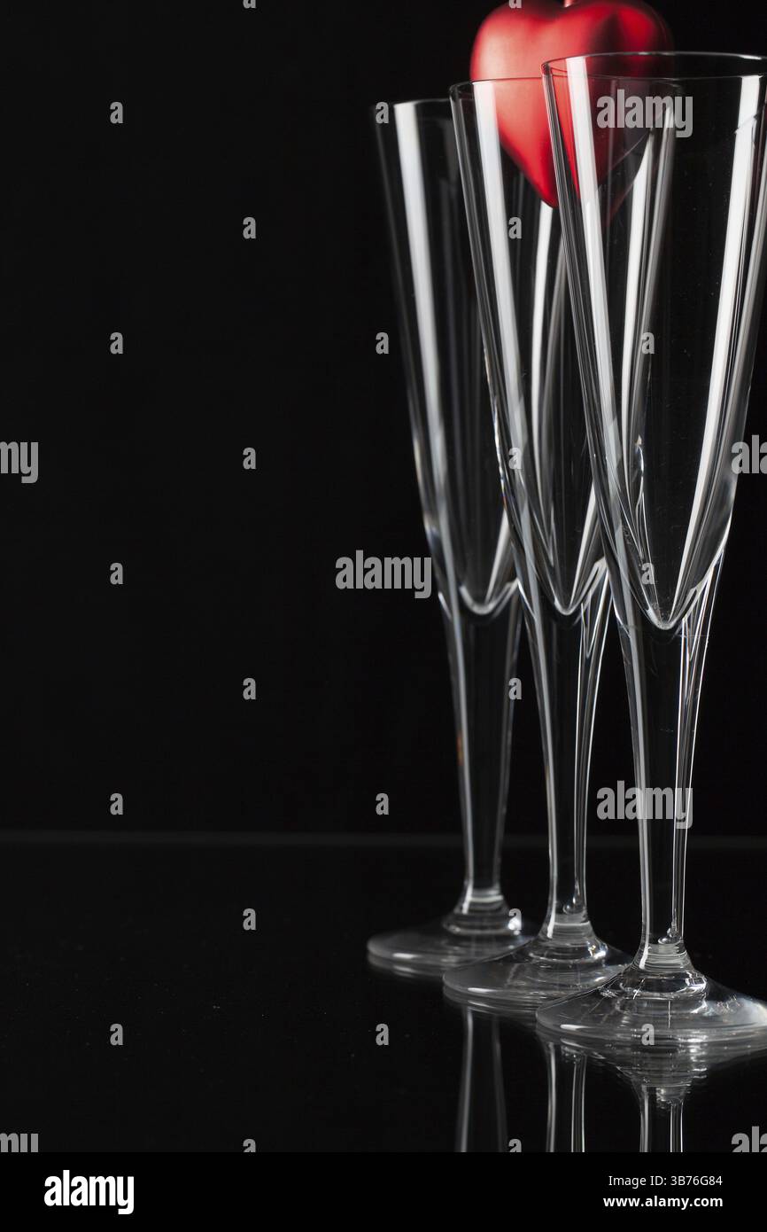 Tre bicchieri di champagne e cuore rosso su una lastra di vetro Foto Stock