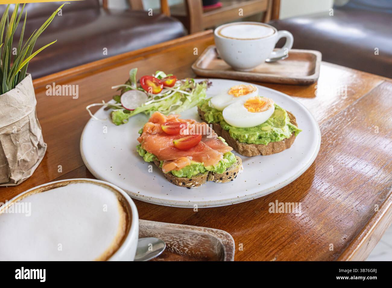 Una deliziosa colazione comprende pane tostato ricoperto di avocado cremoso, fette di salmone affumicato, pomodori ciliegini e un uovo sodo. ACCO Foto Stock