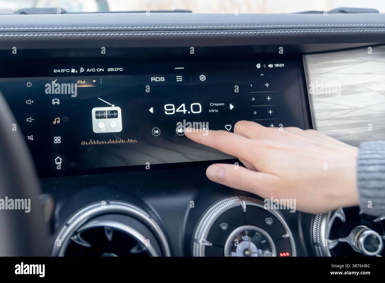 La mano di una donna alza il volume del cruscotto di un'auto moderna. Il cruscotto dell'auto è dotato di un moderno touch screen integrato con una radio sta Foto Stock