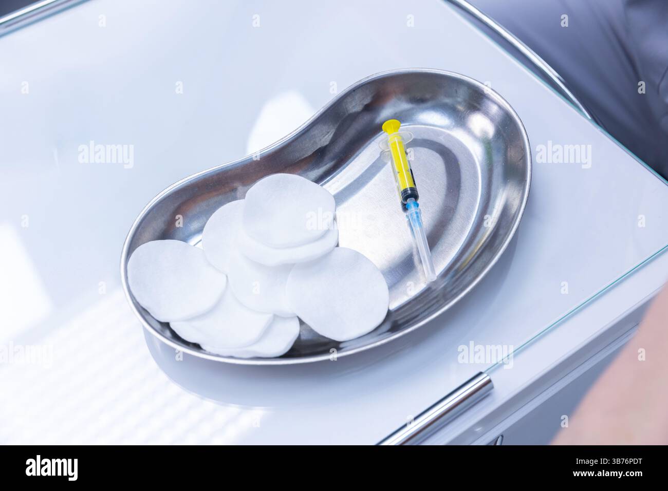 Primo piano di un vassoio in acciaio inossidabile contenente diversi tamponi di cotone e una siringa. Questa configurazione è comunemente utilizzata in ambienti medici per applicazioni igieniche pubbliche Foto Stock