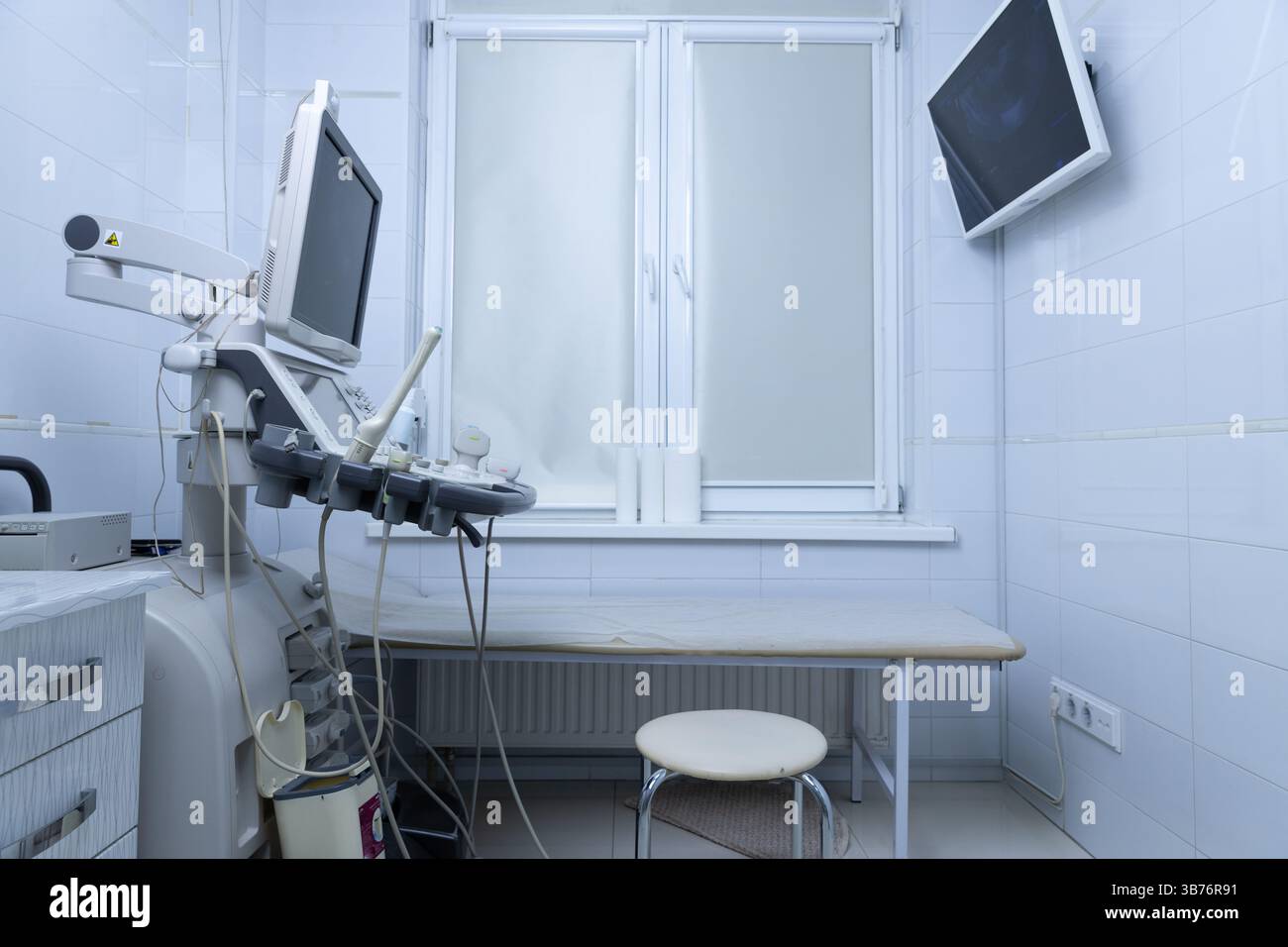 All'interno di una moderna sala esame medica dotata di apparecchiature ecografiche all'avanguardia, un tavolo da visita ordinato e un design minimalista Foto Stock