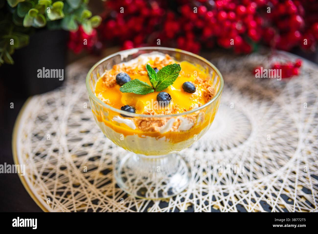 Rinfrescante parfait di mango e mirtilli con panna montata, biscotti sbriciolati e foglie di menta servite in un elegante bicchiere. Foto Stock