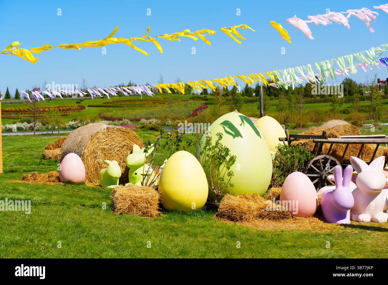 Vivace ambiente esterno con grandi uova di Pasqua color pastello e giocose sculture coniglietto, circondato da balle di fieno e da un bel giardino Foto Stock