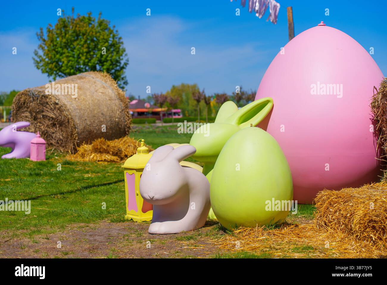 Vivace esposizione di grandi decorazioni pasquali, tra cui coniglietti e uova, ambientate in una soleggiata fattoria all'aperto con balle di fieno e lussureggiante erba verde. Foto Stock