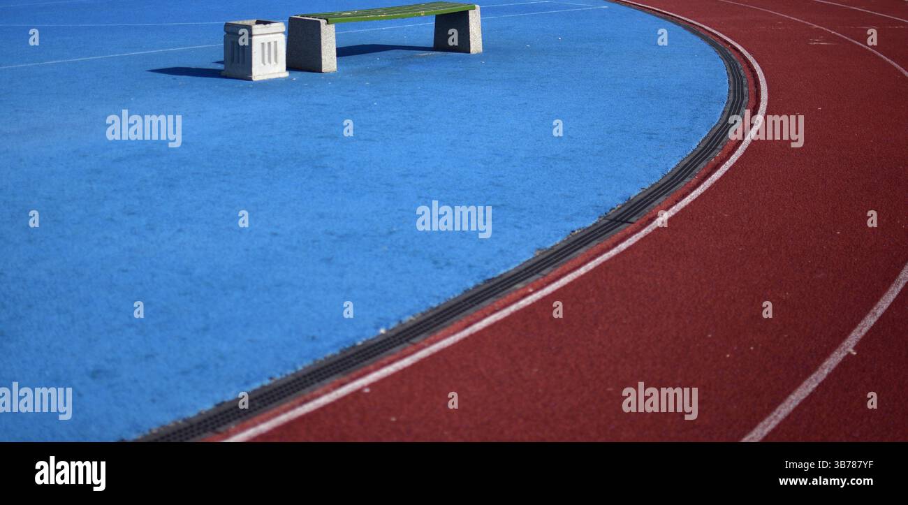 Pista da running rossa con campo sportivo blu e panca nella giornata di sole a sinistra Foto Stock