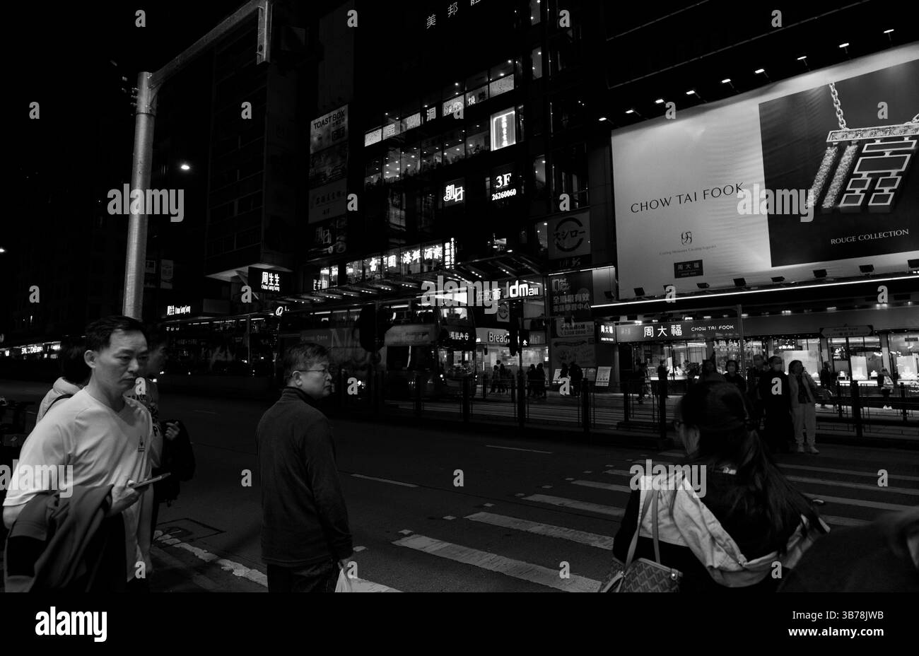 I pedoni notturni si fermano in un vivace incrocio sotto il bagliore dei cartelli al neon Foto Stock