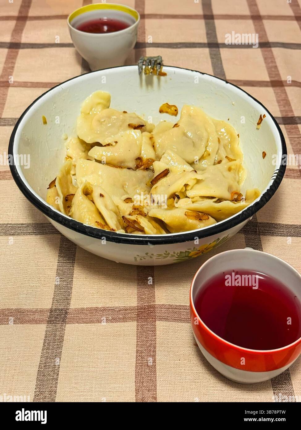 Gnocchi tradizionali con cipolle fritte serviti in una ciotola vintage con bevanda alla frutta, succo di frutta su un tavolo a scacchi. Cucina casalinga, comfort vintage Foto Stock