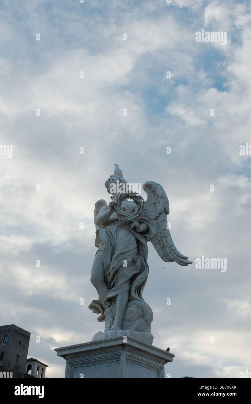 Statue d'angelo barocco sul Ponte Sant'Angelo a Roma con un cielo spettacolare e la classica architettura romana sullo sfondo, monumento culturale e dettagli scultorei. Foto di alta qualità Foto Stock