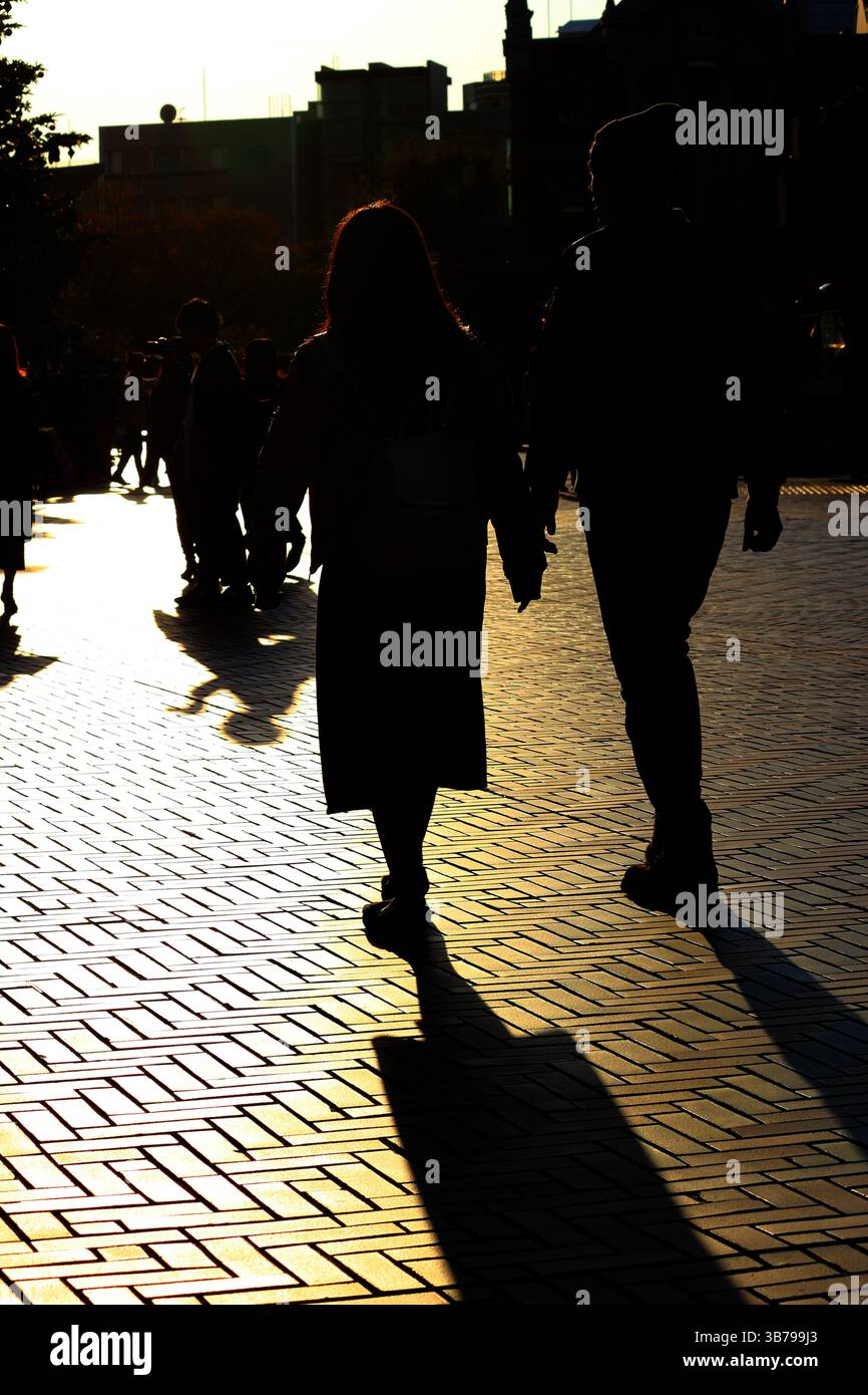 Scene di tutti i giorni in Giappone silhouette di una coppia che cammina attraverso la città alla luce del sole al crepuscolo Foto Stock