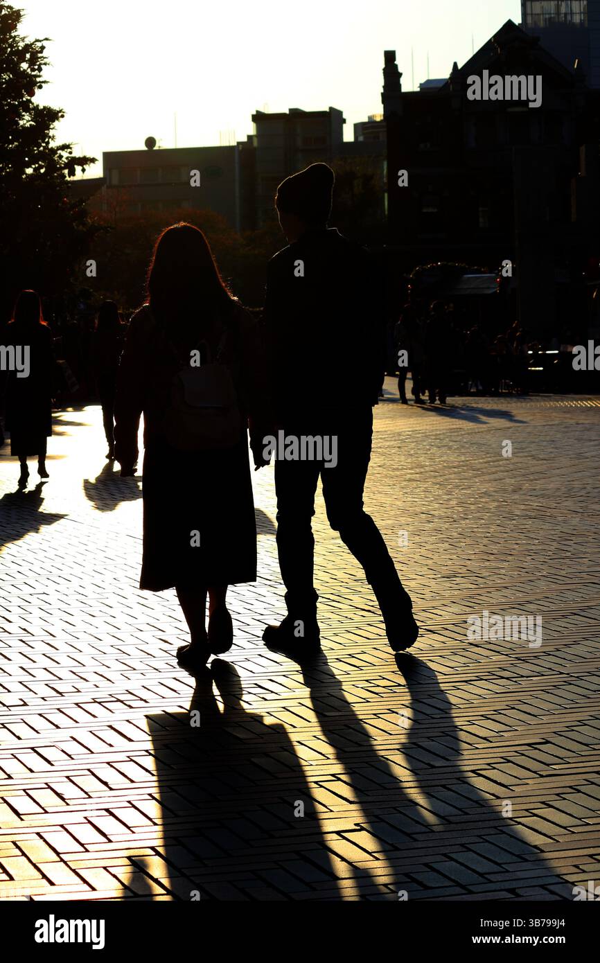Scene di tutti i giorni in Giappone silhouette di una coppia che cammina attraverso la città alla luce del sole al crepuscolo Foto Stock