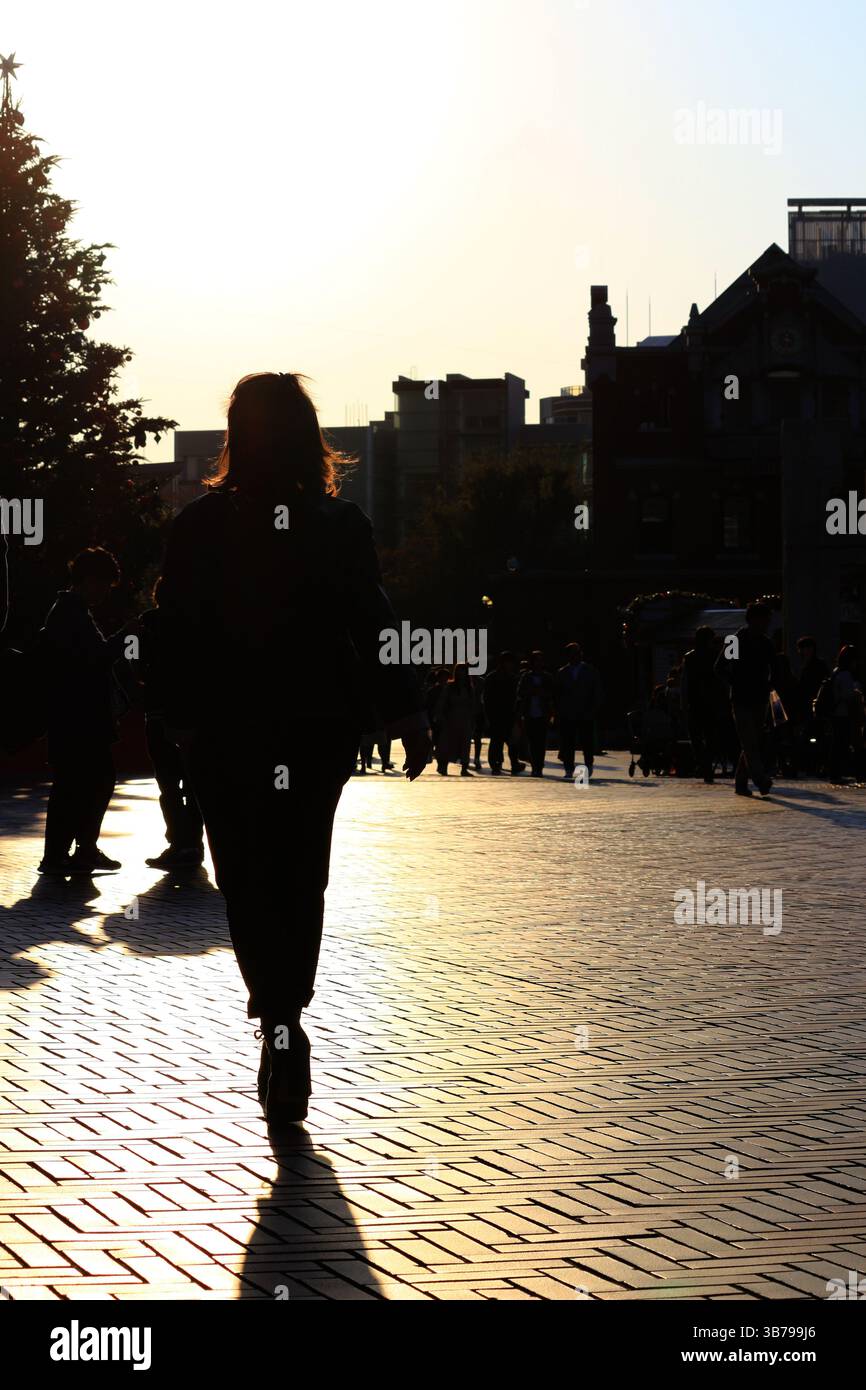 Scene di tutti i giorni in Giappone silhouette di una donna che cammina per la città alla luce del sole al tramonto Foto Stock