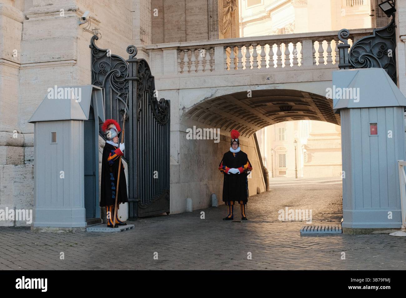 Guardie Svizzere in uniforme rinascimentale tradizionale in piedi alla posta vicino all'ingresso della città del Vaticano con archi storici in pietra e cabine di guardia. Foto di alta qualità Foto Stock