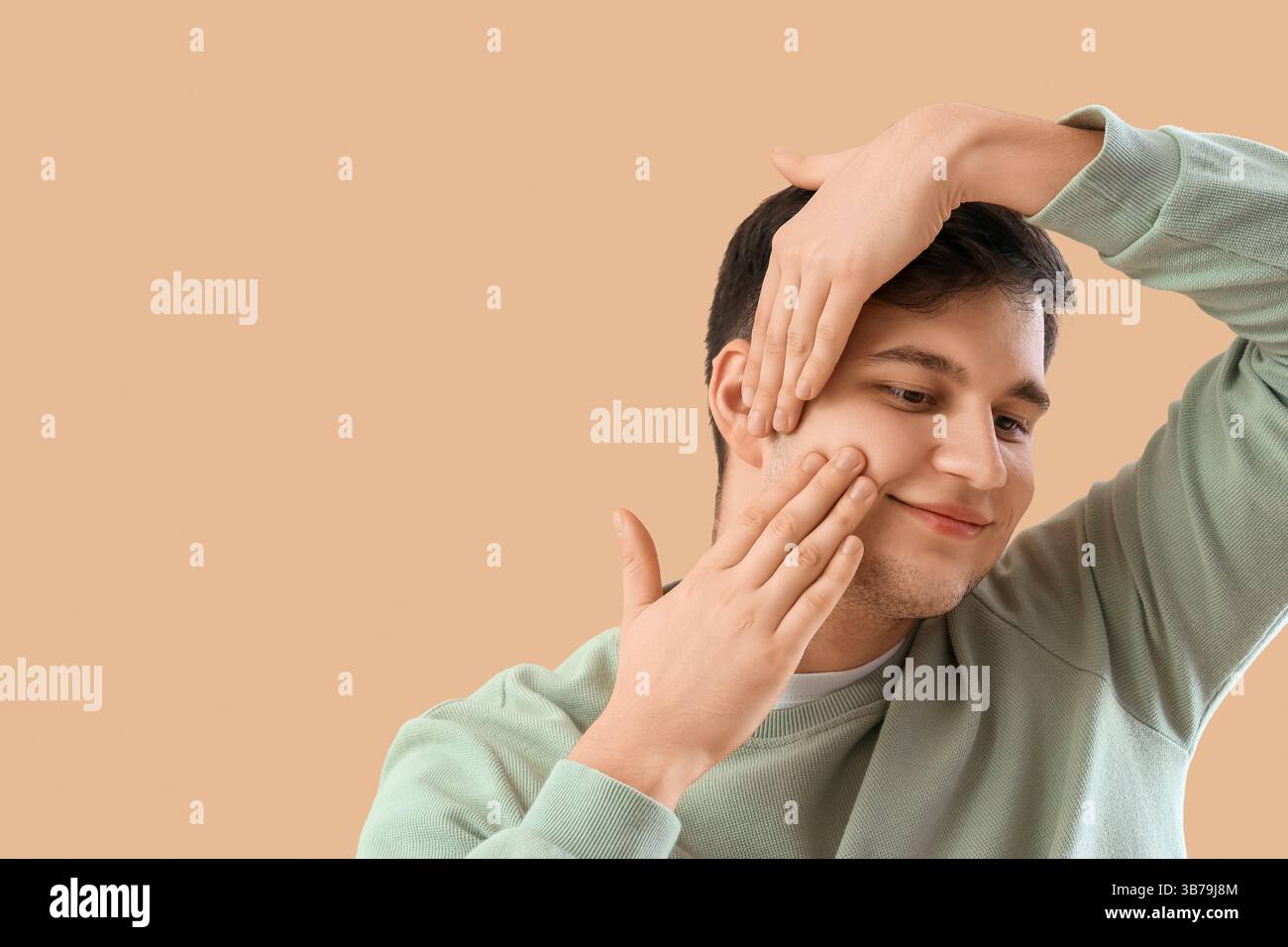 Giovane che fa esercizio di face building su sfondo beige Foto Stock