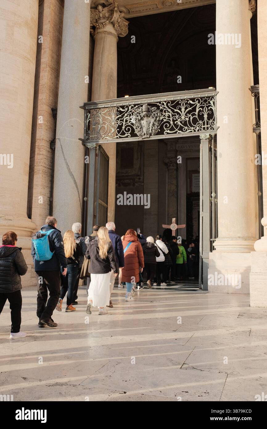 Pellegrini e turisti che entrano nella porta Santa della Basilica di San Pietro nella città del Vaticano attraverso le porte di bronzo ornate durante l'evento del Giubileo dell'anno Santo con croce visibile e raduno spirituale presso il sito sacro cattolico. Foto di alta qualità Foto Stock
