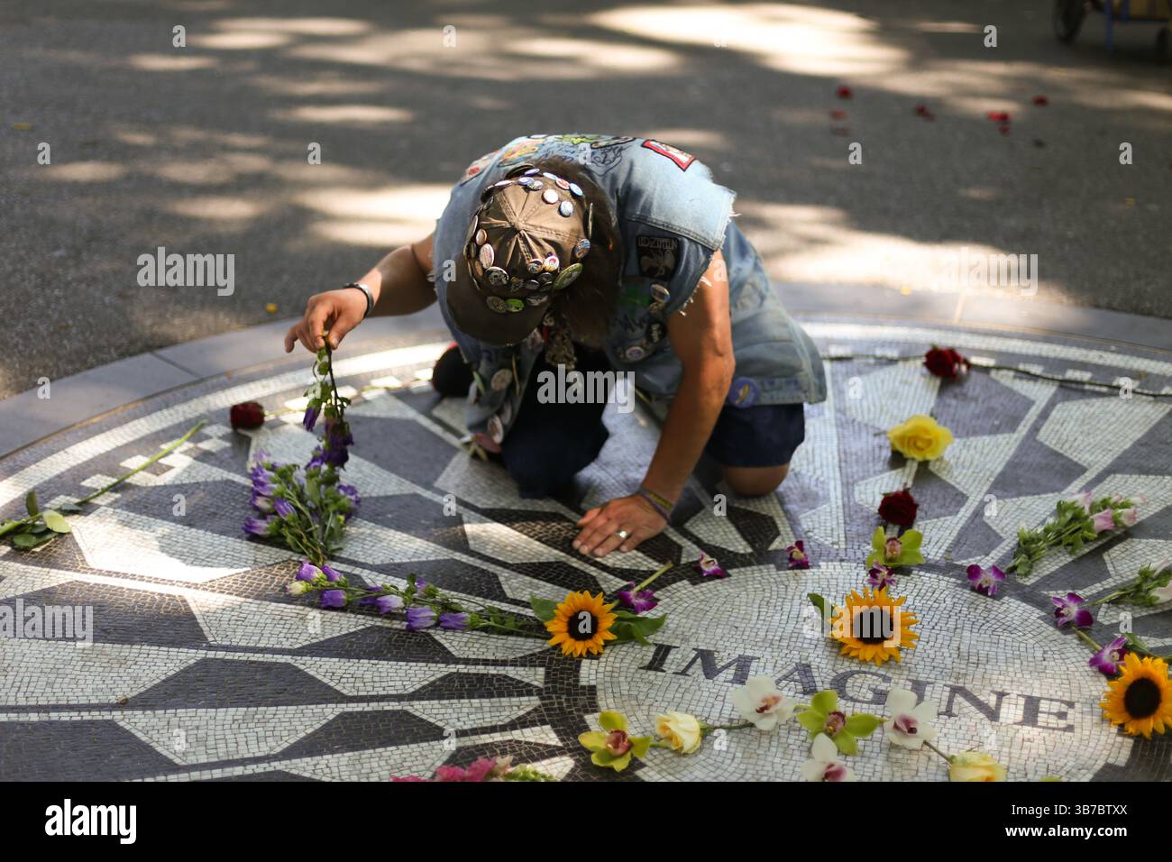 New York City, NY – luglio 2013: Un visitatore colloca fiori intorno al mosaico "Imagine" a Strawberry Fields, in onore dell'eredità di John Lennon. Foto Stock