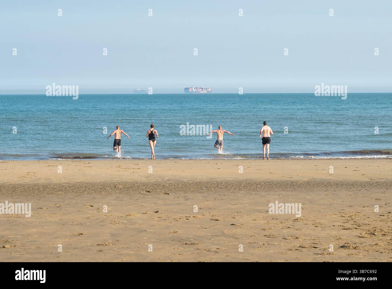 Gruppo di giovani che corrono in mare, Sandown, Isola di Wight, Regno Unito Foto Stock