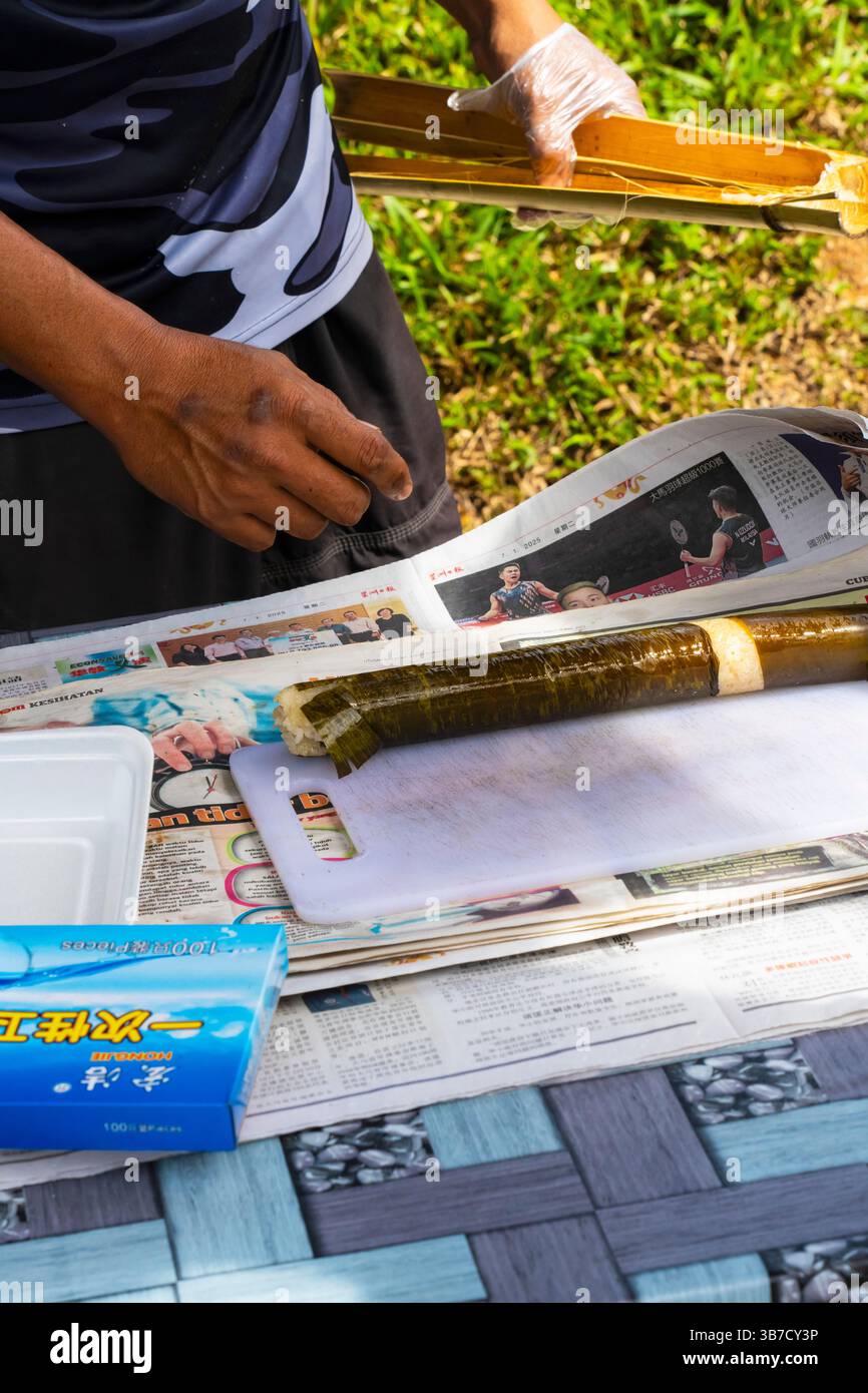 Uomo malese che cucina riso in tubo di bambù. Si chiama anche riso di bambù o riso di bambù fragrante, Malesia. La morbidezza e la freschezza del torrefatto Foto Stock