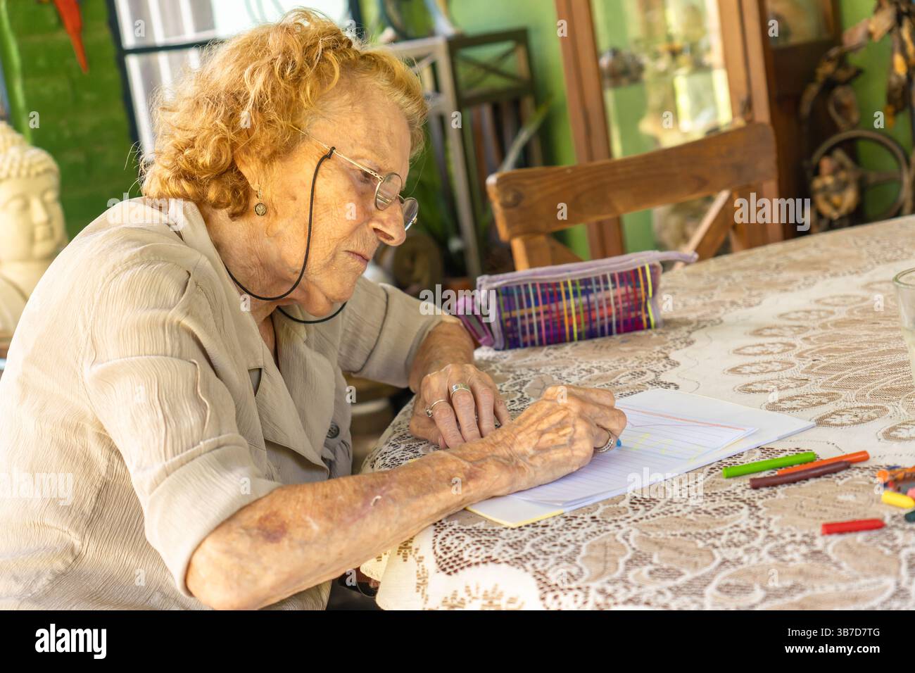 Una donna anziana siede a un tavolo, travolto dal disegno con pastelli, dimostrando un appagante pensionamento impegnandosi in attività creative a casa Foto Stock