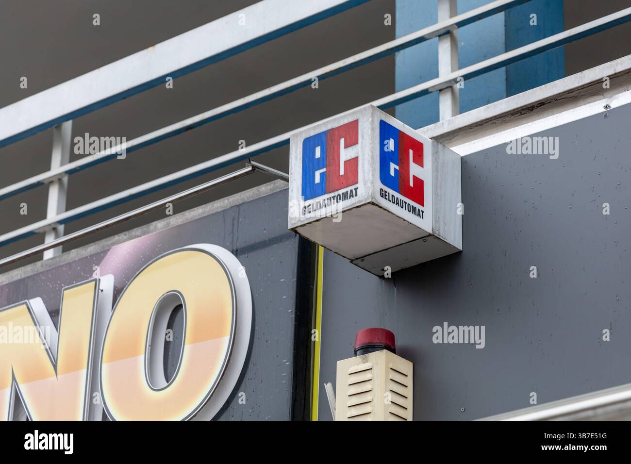 Un cartello a forma di cubo "Geldautomat" (ATM) con accenti rossi e blu è montato su una parete grigio scuro. indica un'ubicazione del bancomat. Berlino, Germania. Foto Stock