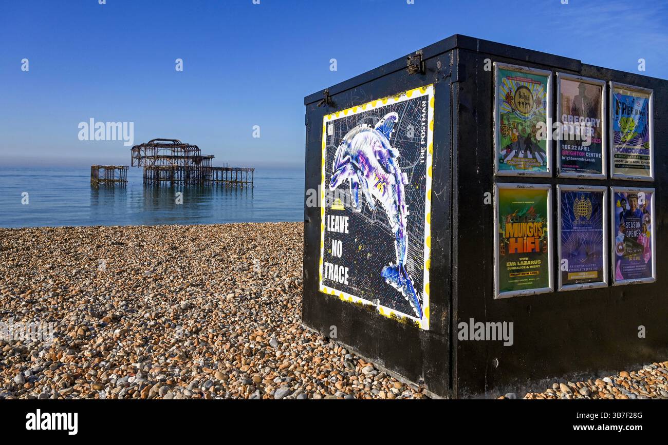 Il molo e la spiaggia di Brighton West con un poster del Postman che chiede ai visitatori di portare via la loro cucciolata in una bella mattinata di sole, nel Sussex UK Foto Stock
