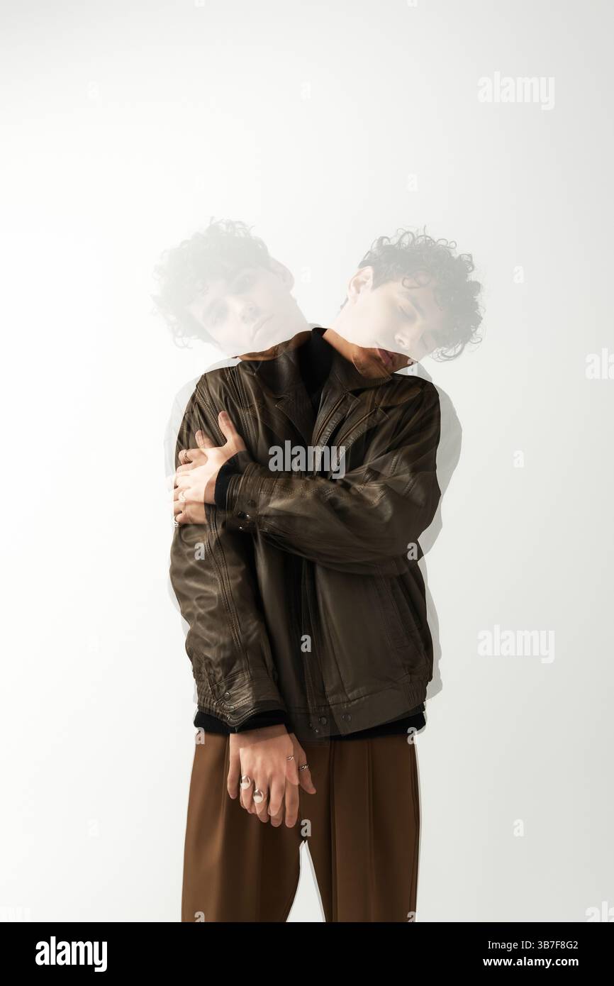 Un giovane uomo con un'elegante giacca in pelle marrone mostra un movimento artistico con le braccia incrociate. Foto Stock