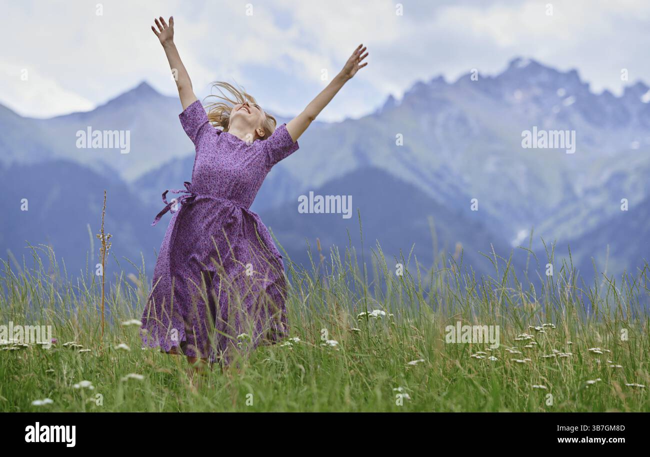 Una donna bionda felice con le braccia alzate gode della natura nel prato di montagna, Stati Uniti, Nord America Foto Stock
