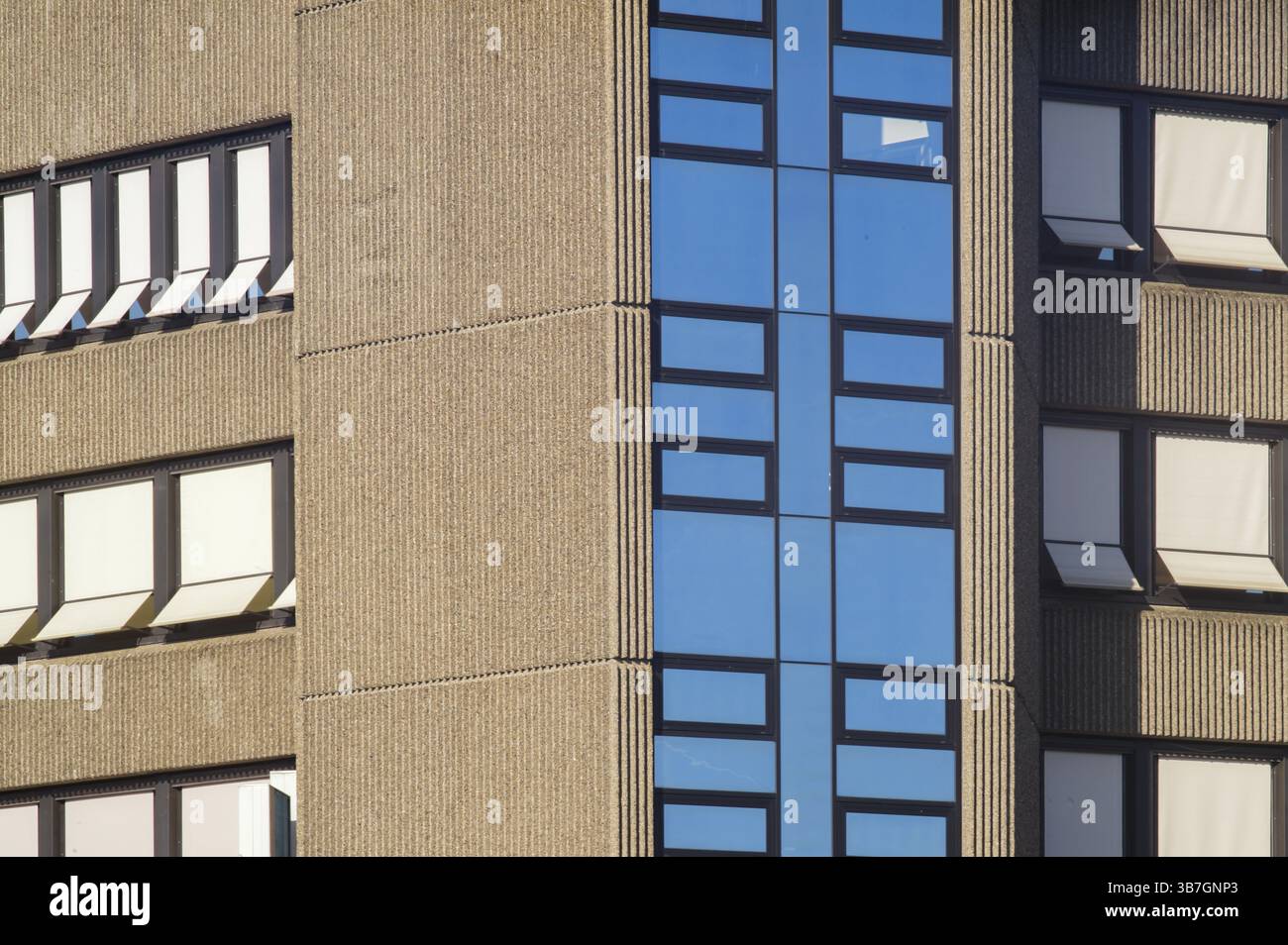 Facciata in cemento di un edificio moderno con finestre tendaloni, alcune aperte e alcune chiuse, che riflettono il cielo blu Foto Stock