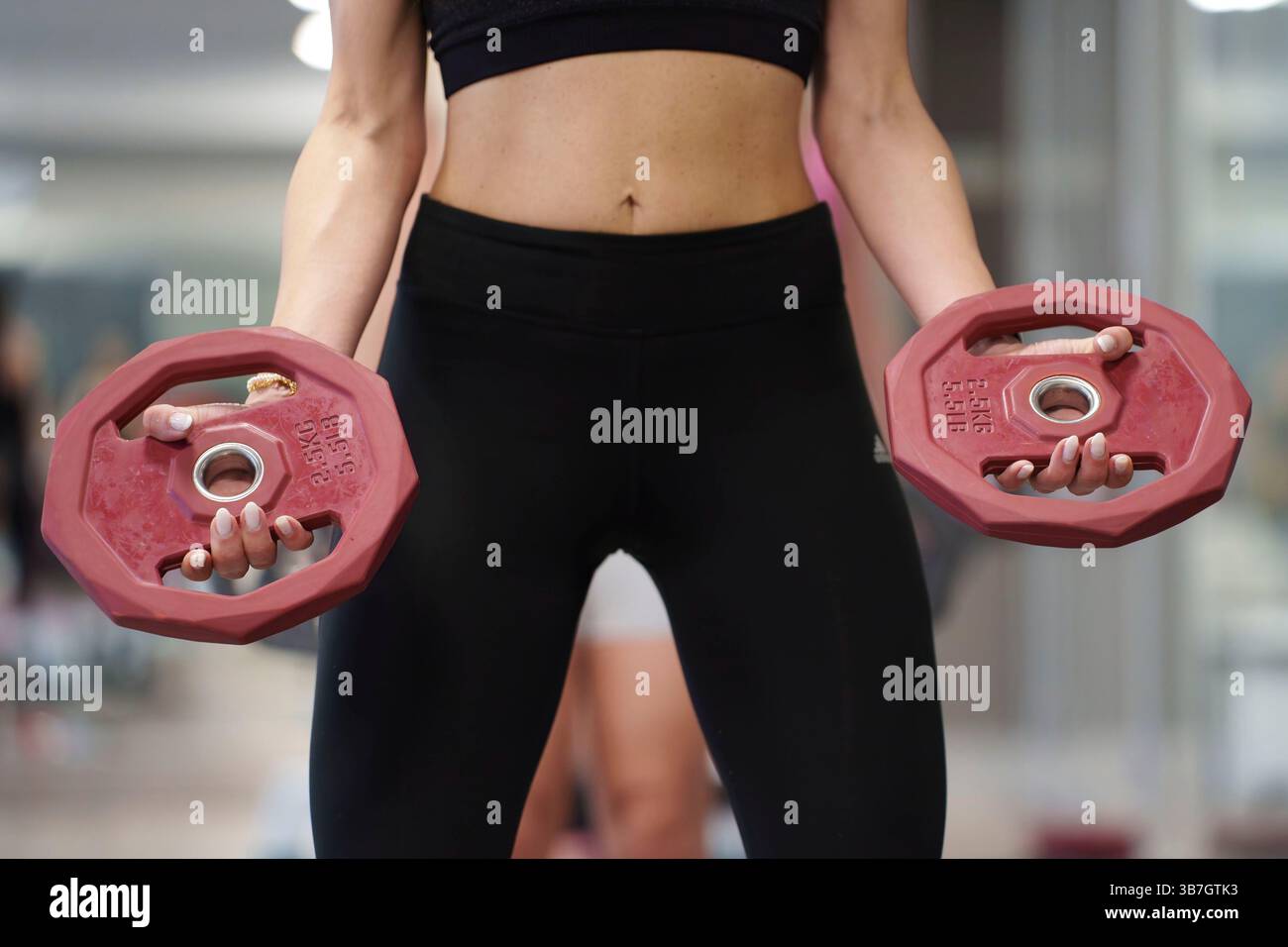 Donna in palestra con due pesi rossi mentre esegue un esercizio di forza in una palestra Foto Stock