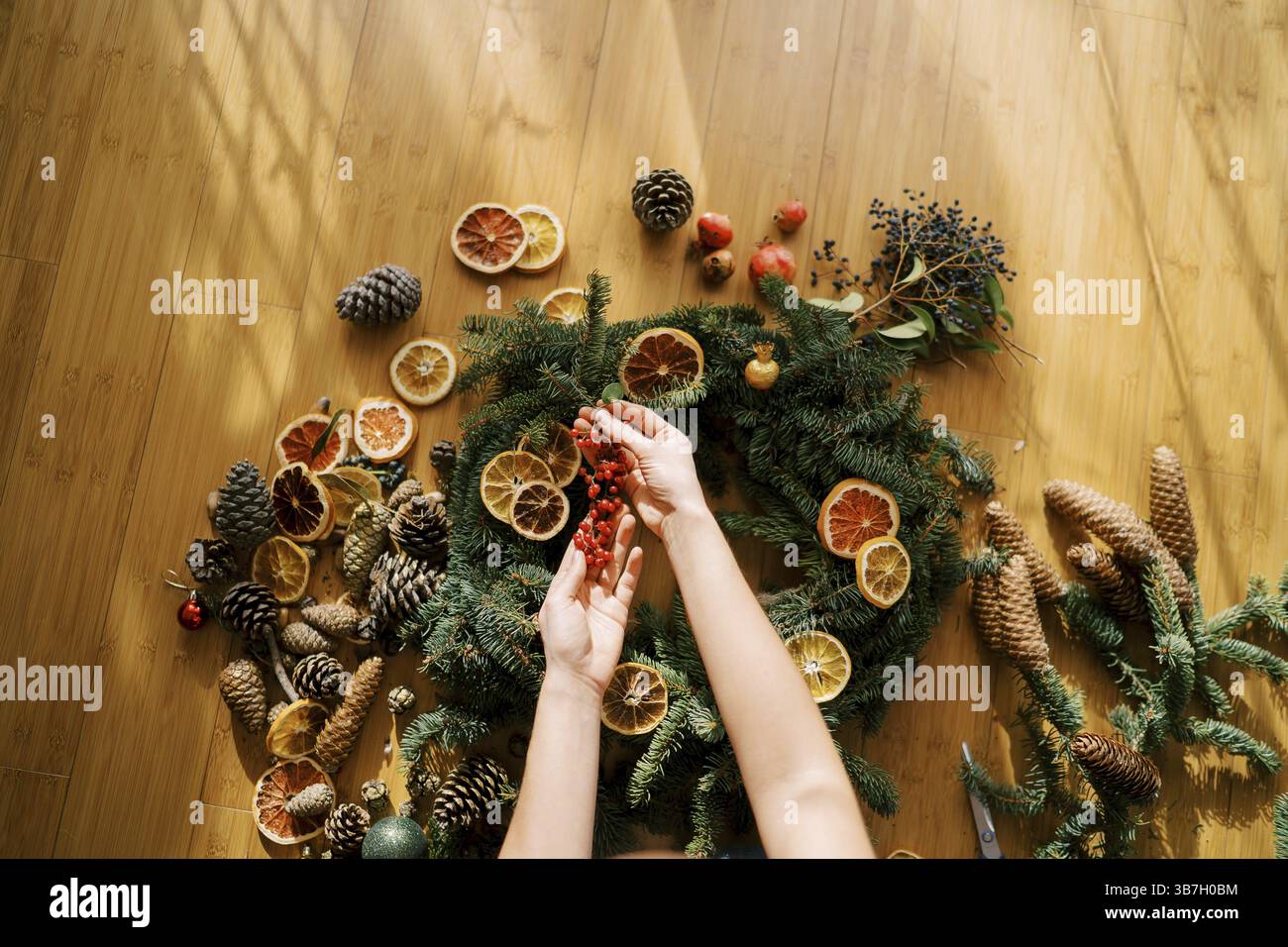 Le mani delle donne tengono un rametto di bacche rosse su una corona di Natale stesa sul pavimento. Vista dall'alto. Foto Stock
