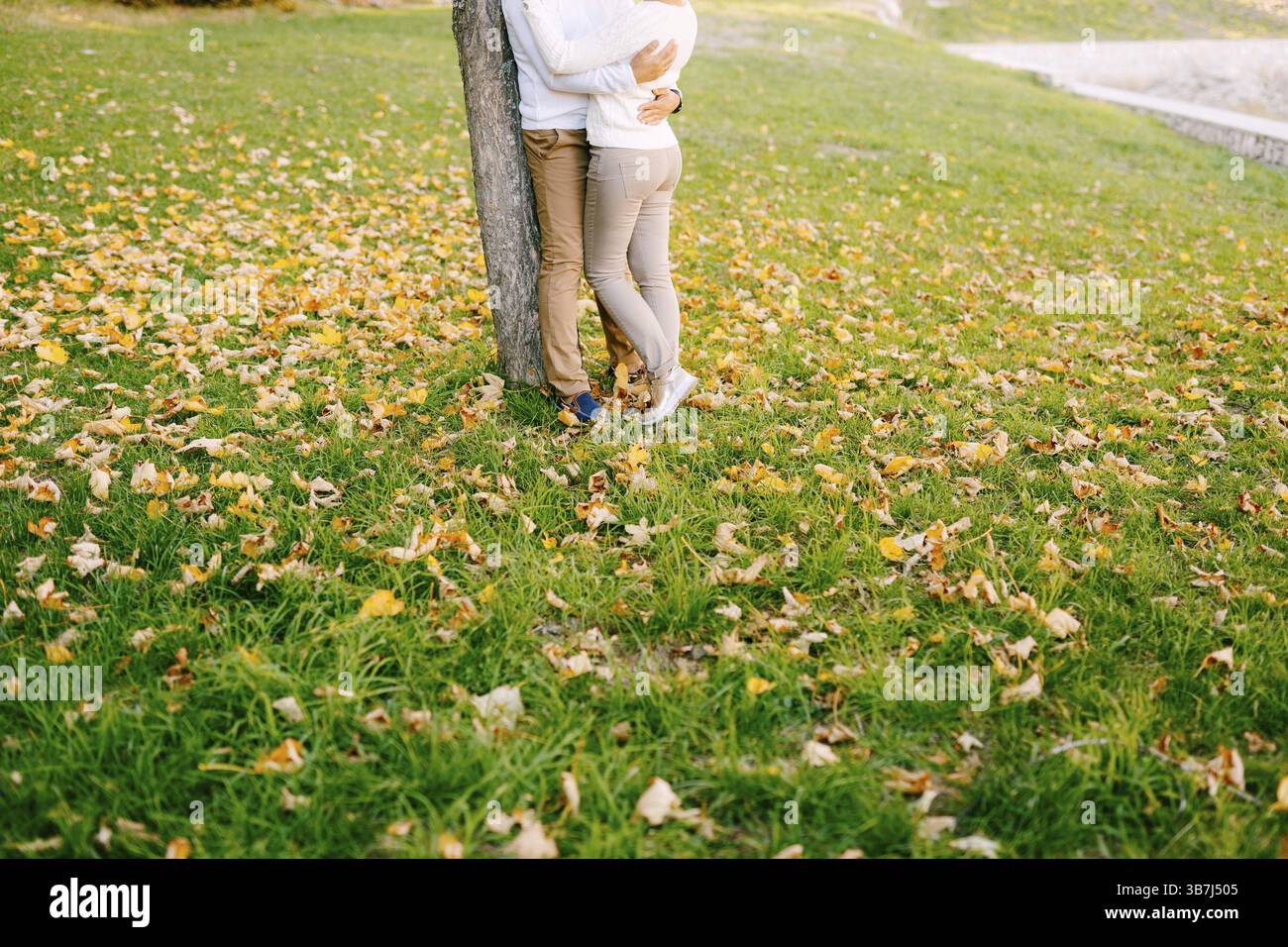 L'uomo abbraccia la donna in pantaloni beige su uno sfondo verde nella foresta autunnale. Primo piano. Foto Stock