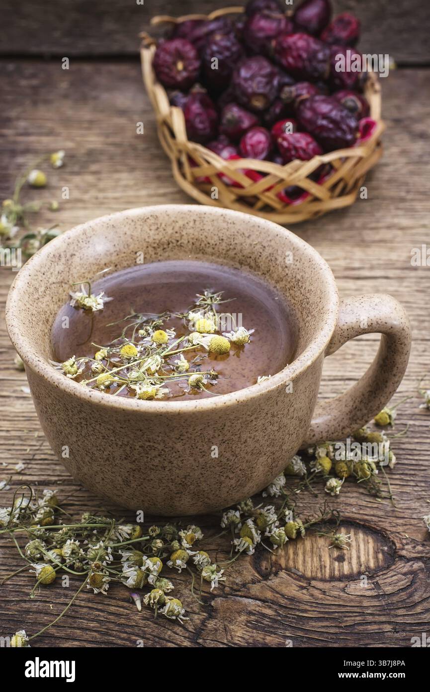 Tazza in ceramica preparata con rosa fianchi e camomilla in stile rustico vintage Foto Stock