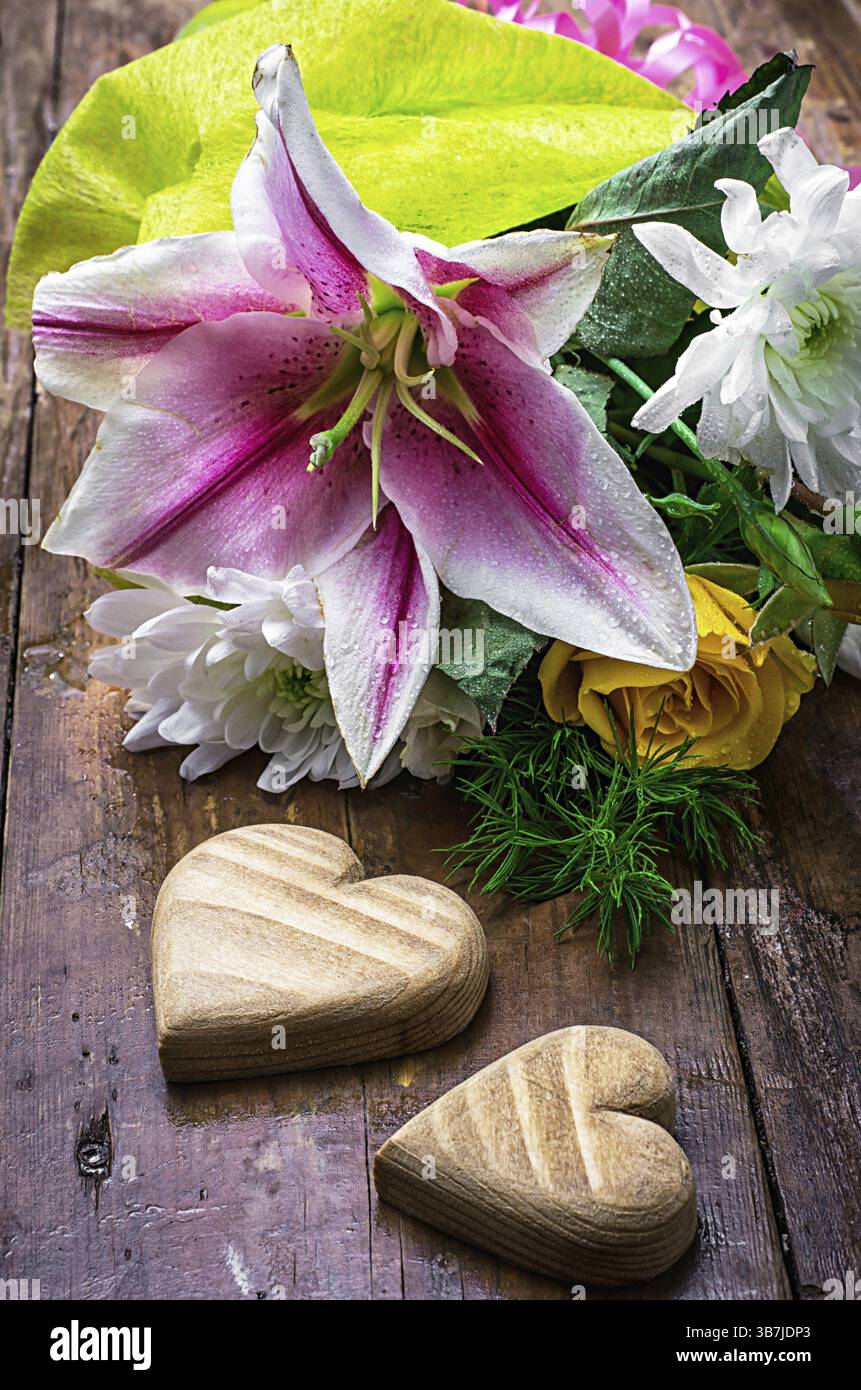 Cuore simbolico in legno intagliato a mano su mazzi di fiori sullo sfondo Foto Stock