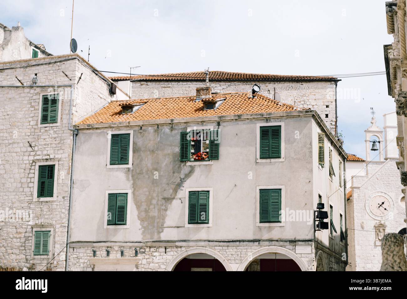 Vecchio edificio residenziale a tre piani con persiane verdi e piastrelle arancioni sul tetto. Foto Stock