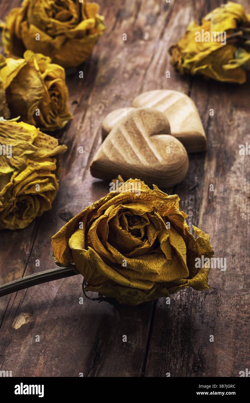 Cuore simbolico in legno intagliato a mano su uno sfondo di rose gialle Foto Stock