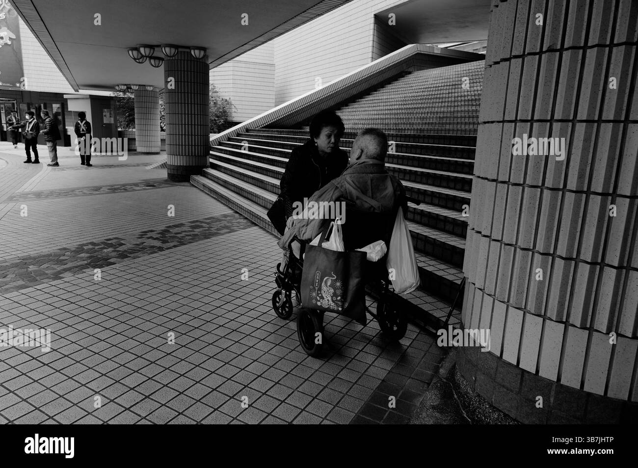 La donna si appoggia dolcemente per parlare con un uomo su una sedia a rotelle fuori dal Centro culturale di Hong Kong Foto Stock