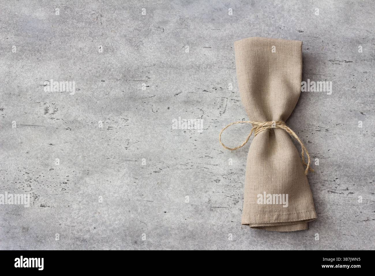 Vista dall'alto del tovagliolo in lino piegato legato con la corda su una superficie in pietra ruvida grigia. Tavolo rustico minimalista per lo styling degli alimenti, design ecologico o. Foto Stock