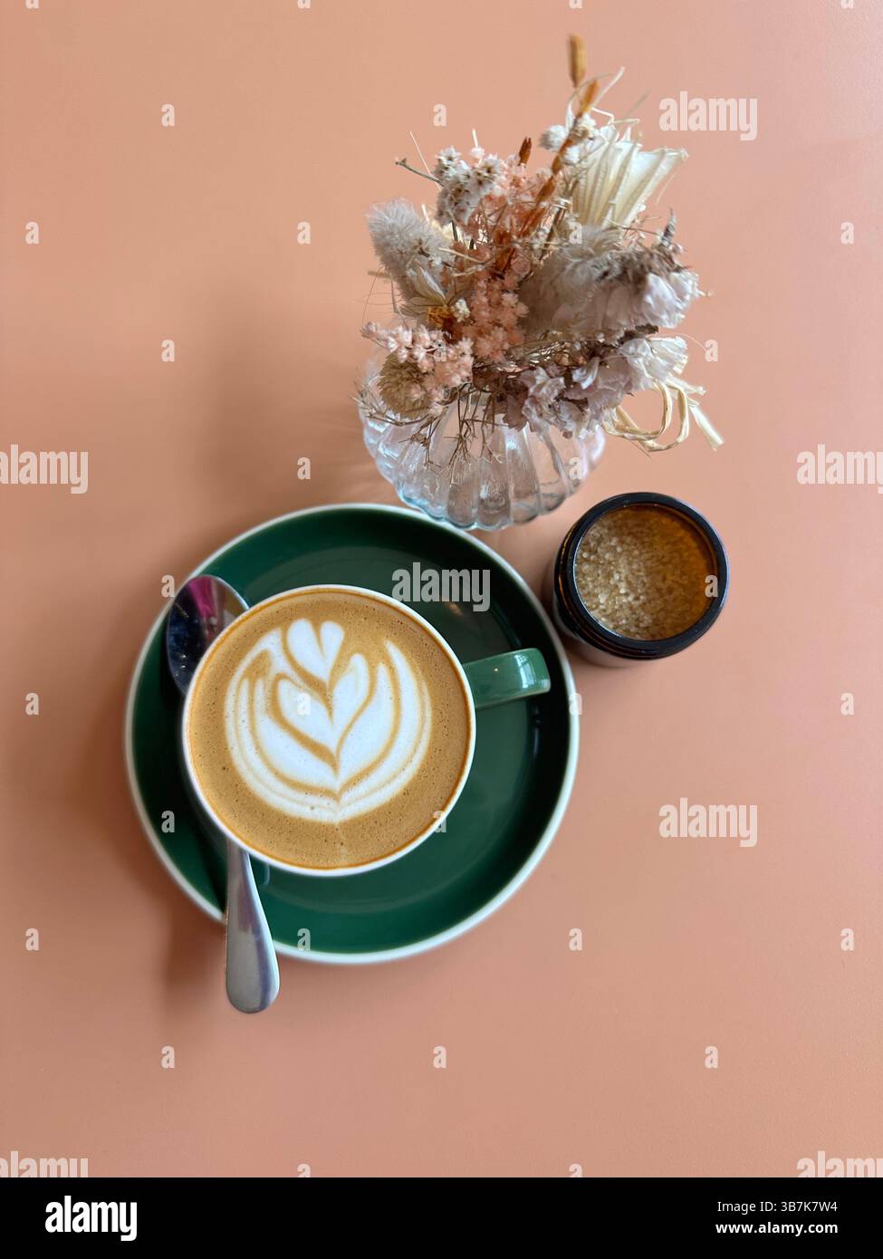 Caffè bianco piatto con cucchiaio, fiori secchi e zuccheriera sul tavolo delle pesche, composizione sopraelevata. - Immagine stock catturata con smartphone