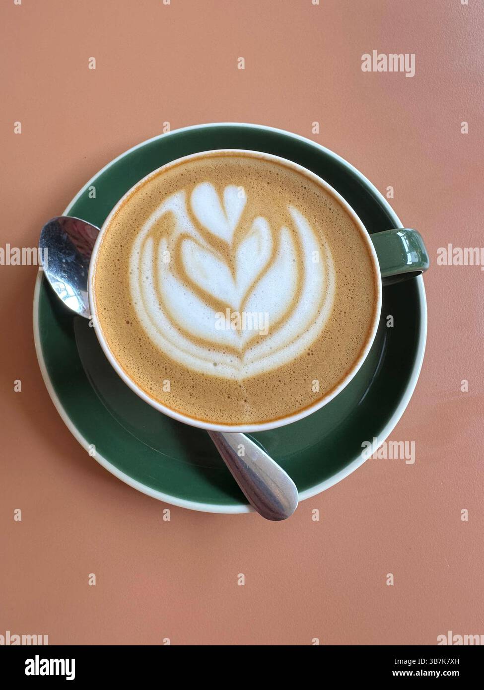 Caffè bianco piatto con latte art in tazza verde e piattino con cucchiaio, sopra il tavolo delle pesche. - Immagine stock catturata con smartphone