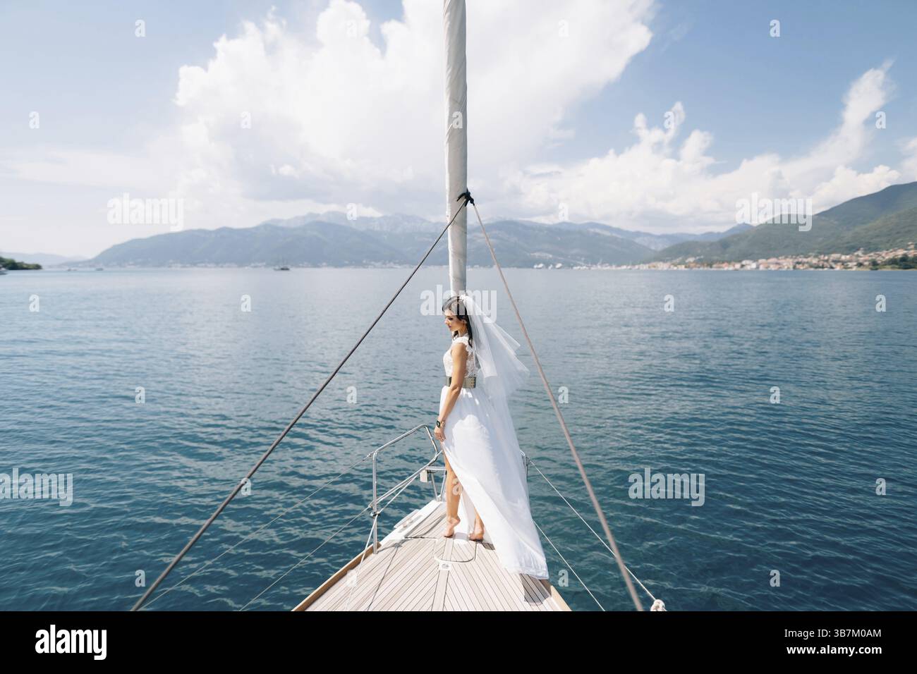 La sposa si erge sulla prua dello yacht che naviga nella baia di Cattaro, vista sul retro. Foto Stock