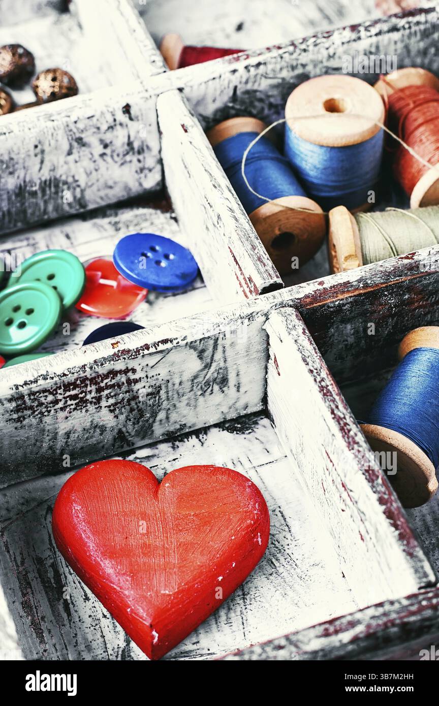 Scatola da cucire in legno con fili, bottoni e cuore simbolico Foto Stock