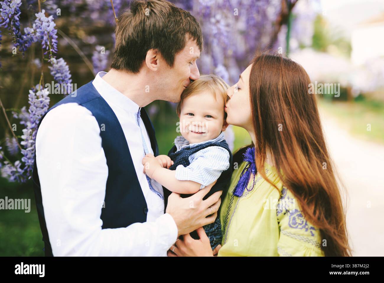 Madre e padre baciano il loro bambino dai capelli rossi. Foto Stock