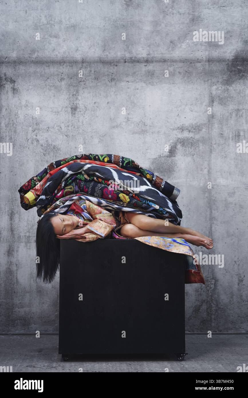 Bella donna addormentata su un cubo nero e coperta da coperte colorate Foto Stock