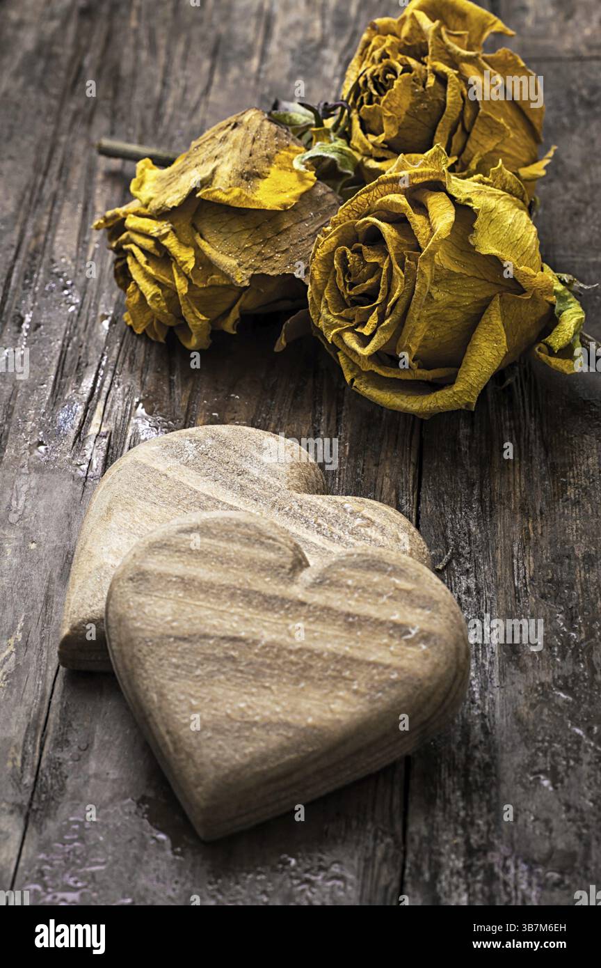 Cuore simbolico in legno intagliato a mano su uno sfondo di rose gialle Foto Stock