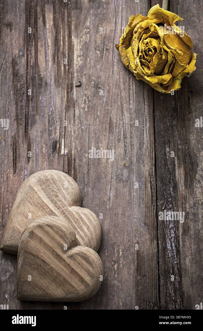 Cuore simbolico in legno intagliato a mano su uno sfondo di rose gialle Foto Stock