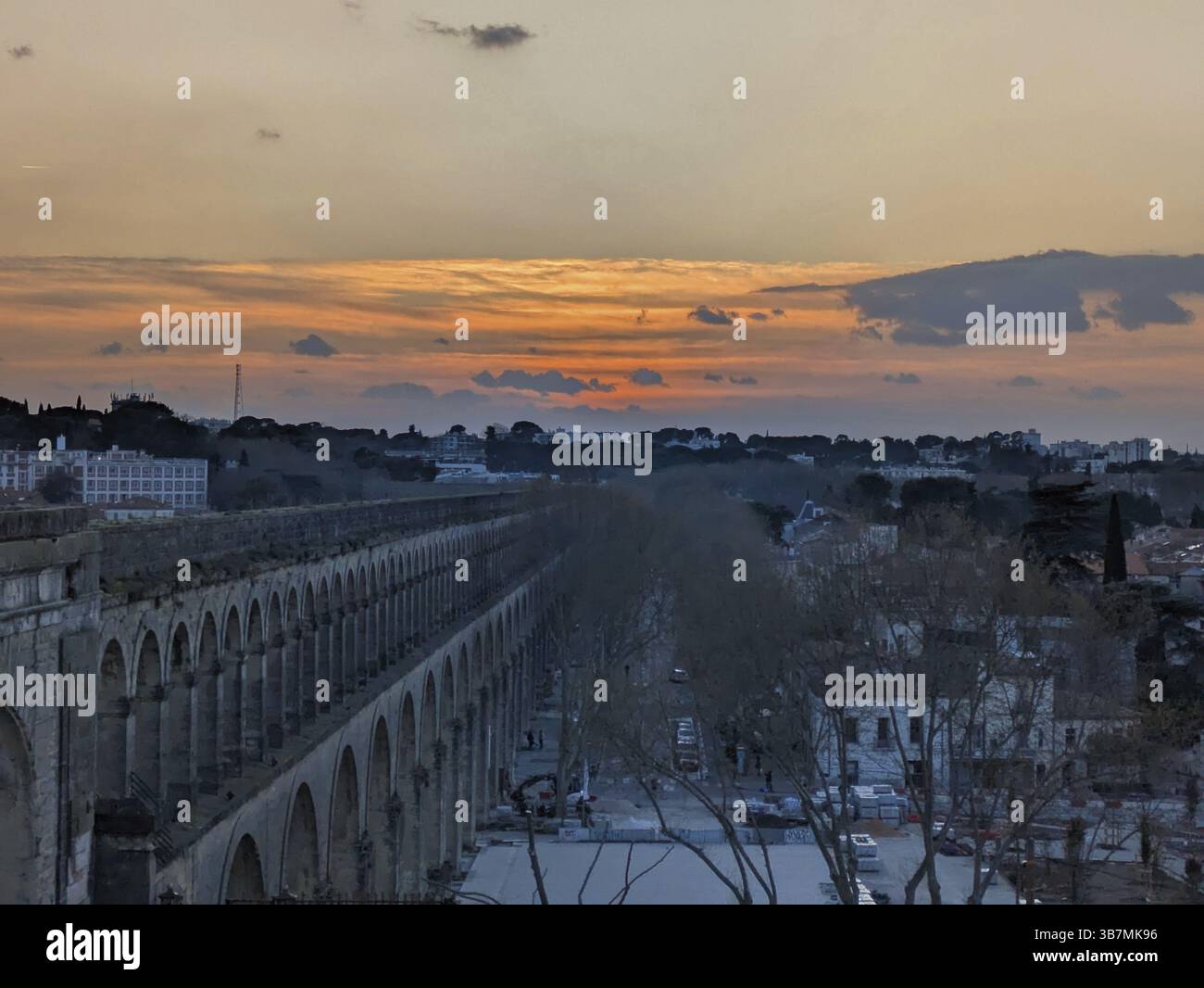 Tramonto sullo skyline della città con un acquedotto e alberi sagomati che offrono uno sfondo tranquillo. Montpellier, Herault, Francia, Europa Foto Stock